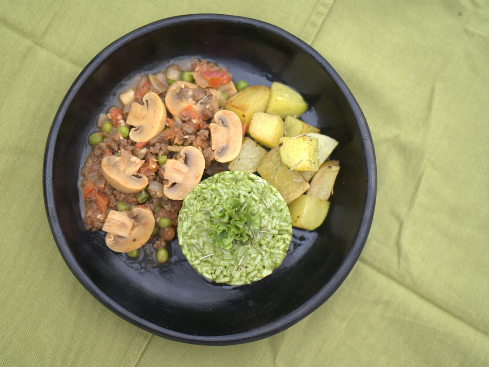 Plato de la cocina de Romero en su primera sesión de fotos: arroz verde, guiso de hongos y papas en un bowl negro sobre mantel verde.