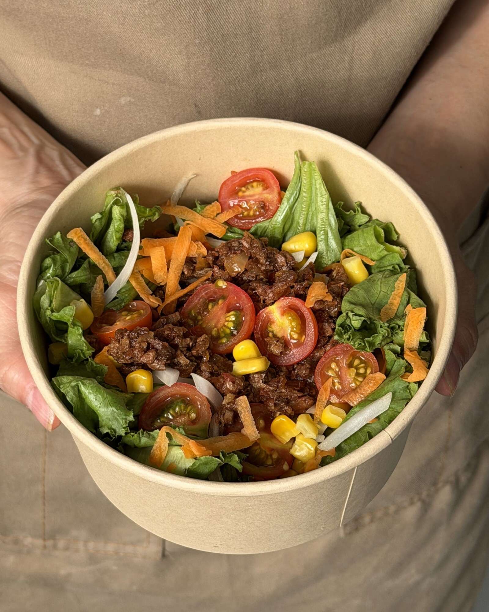 Bowl & Bloom en su envase de papel kraft: lechugas, tomate cherry, maíz, zanahoria y albóndigas plant based.