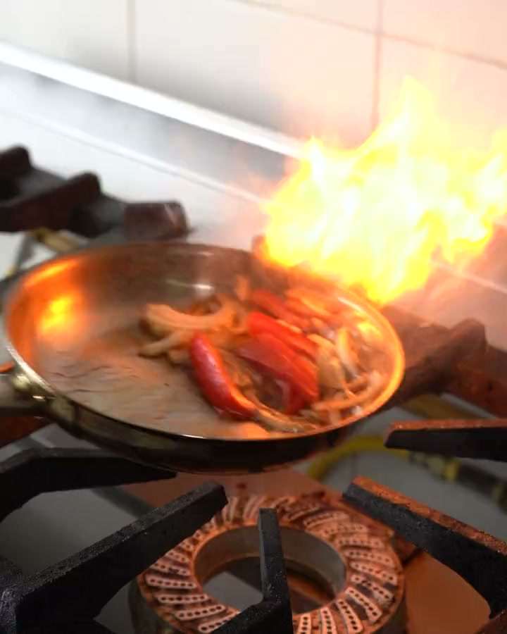 Una sartén con pimientos y cebolla flameando sobre la hornilla, en la cocina de Romero.