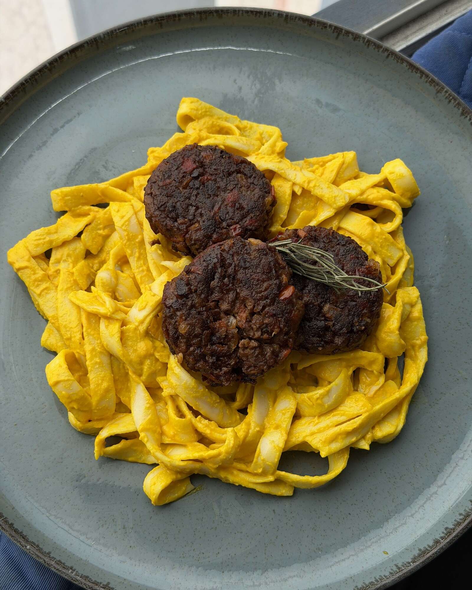 Fettuccini amarillo a la huancaína con tres croquetas de soya y una ramita de romero, en un plato verde.