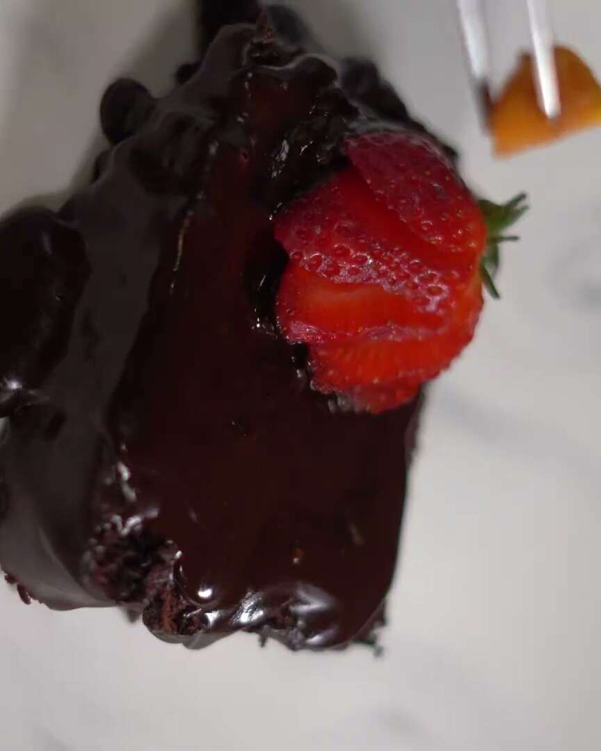 Porción de torta de chocolate bañada en ganache, con una fresa encima.