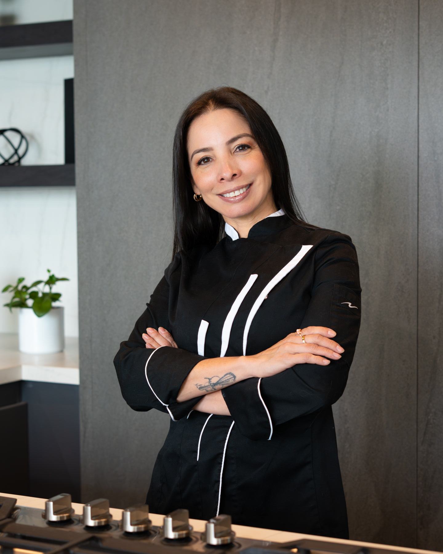 Juliana Romero con chaqueta de chef negra y los brazos cruzados, de pie detrás de una cocina a gas.
