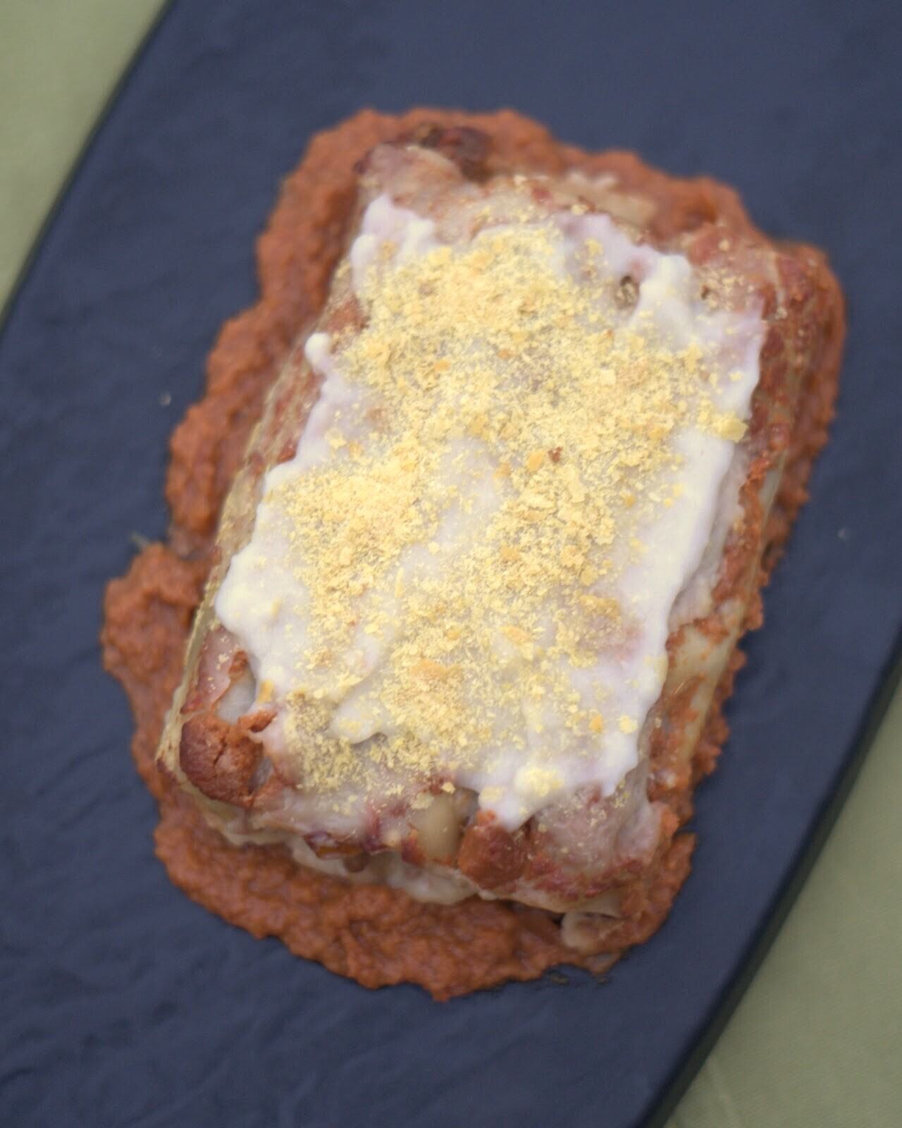 Lasaña de masa de maíz con boloñesa de la casa y bechamel de cashews, vista desde arriba sobre una bandeja azul.