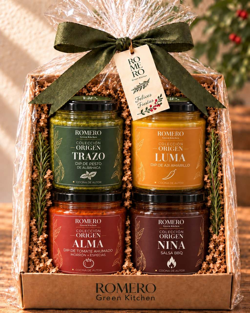Caja de cuatro de la Colección Origen envuelta en celofán con lazo verde y etiqueta de Romero: frascos de Trazo, Luma, Alma y Nina sobre papel kraft.