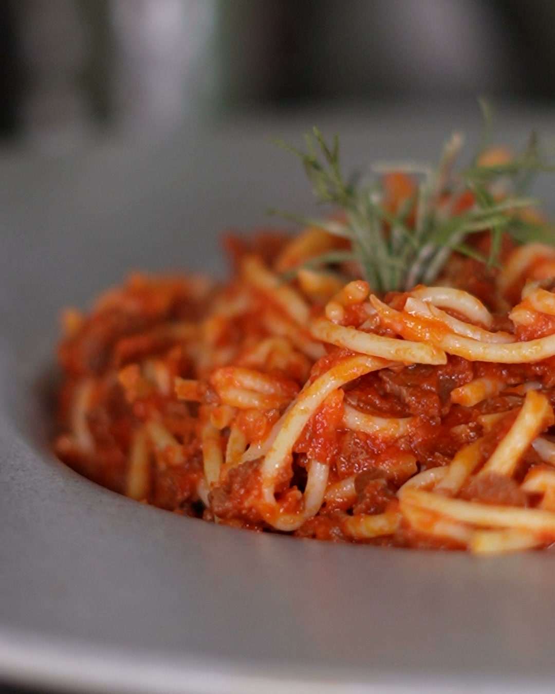 Spaghetti boloñesa de maíz en un plato hondo gris, con una ramita de romero encima.