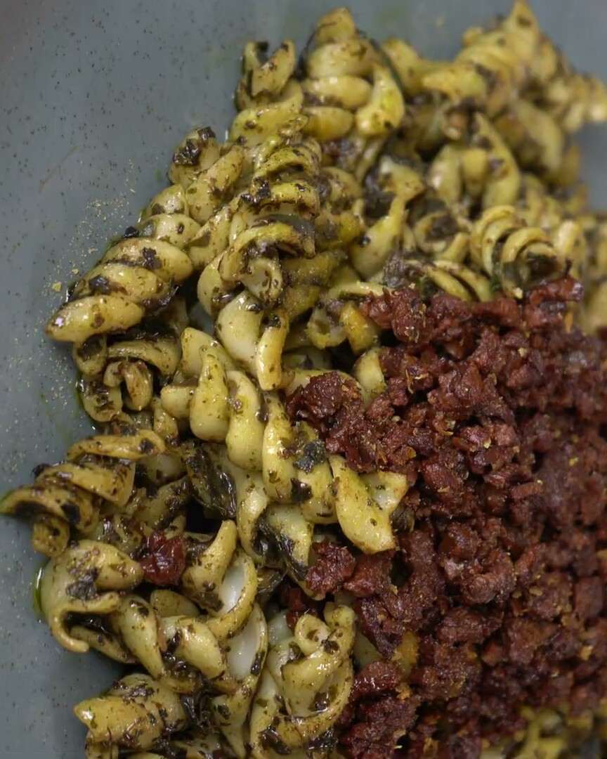 Pasta corta de maíz al pesto en un plato verde, servida con boloñesa de la casa.