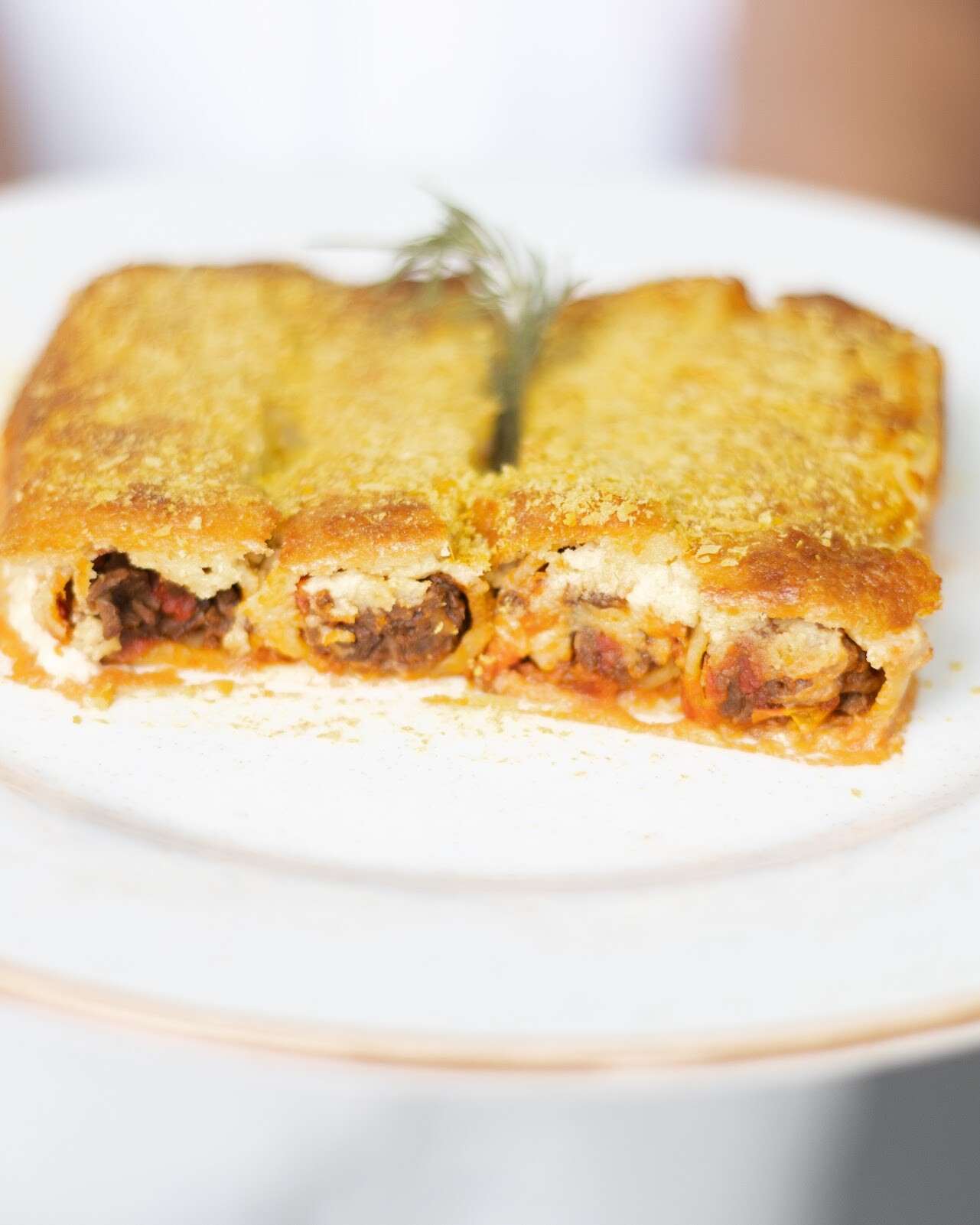 Porción de lasaña de maíz gratinada, con una ramita de romero, en un plato blanco.