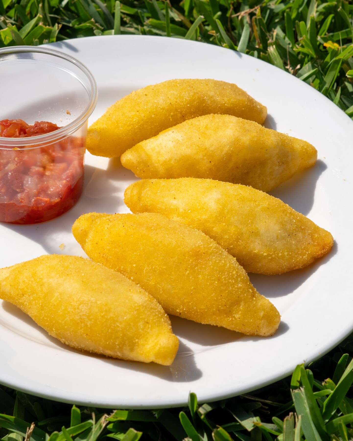 Cinco empanadas de maíz doradas en un plato blanco, con un pocillo de hogao de tomate.